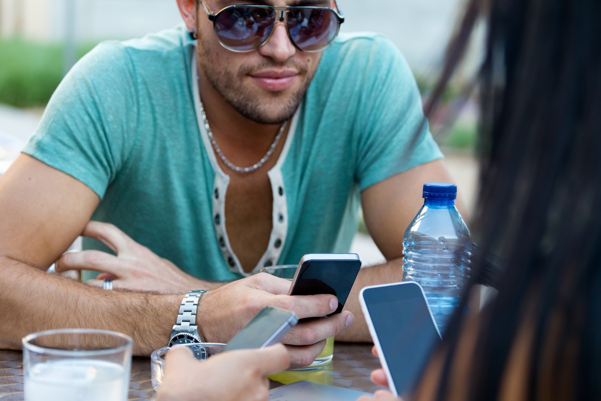Homme en terrasse avec smartphone et amis profite d'un nouveau forfait sur le réseau de SFR