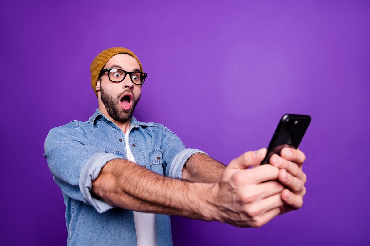 Homme à bonnet sur fond violet, bouche ronde de surprise devant son smartphone à cause du super forfait de YouPrice
