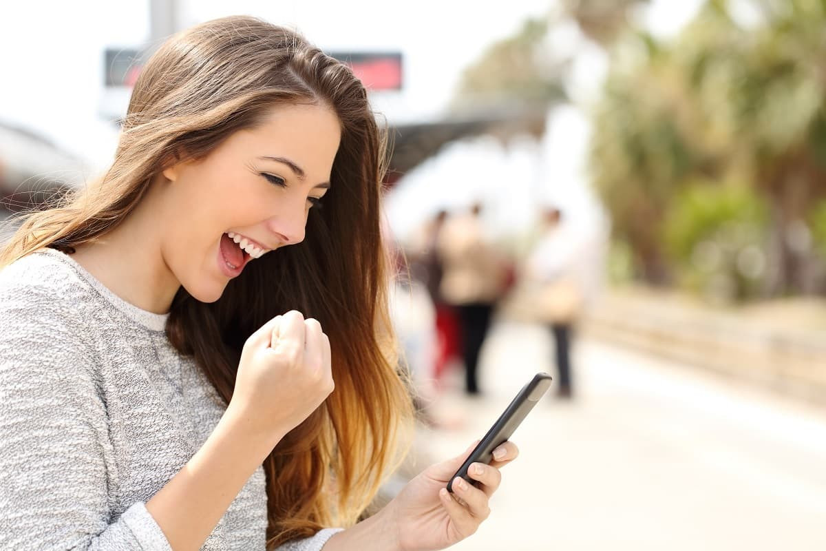Femme sourit et serre le poing de joie devant les remises de Bouygues sur ses smartphones, toutes marques confondues